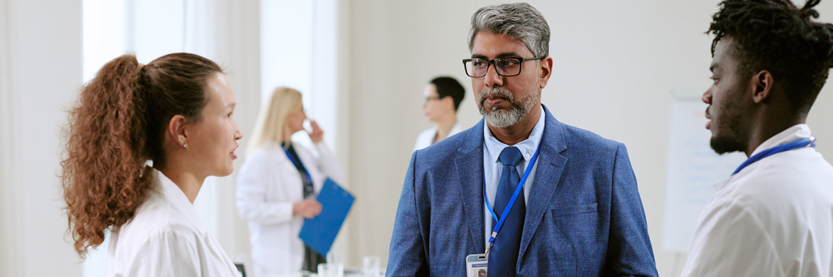 two health care clinicians wearing white coats talking with man in business suit